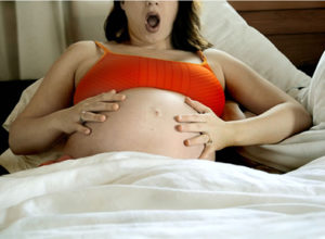 Беременная в постели держится за живот
