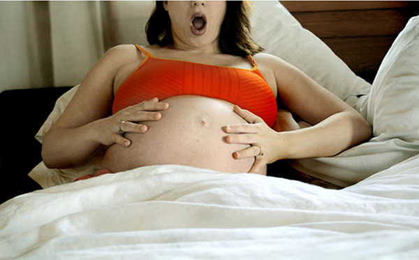 Беременная в постели держится за живот